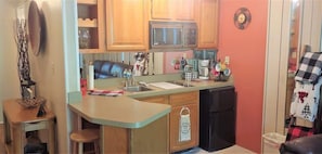 Una cocina funcional con armarios de madera, microondas, cafetera y pileta.