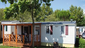 Uma casa móvel com varanda, uma área de estar coberta ao ar livre e uma pequena construção anexa.