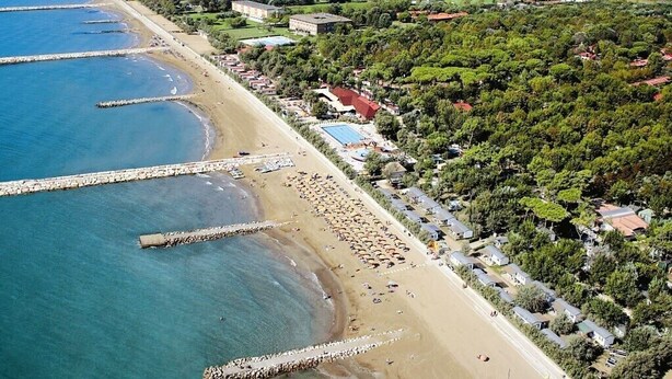 Vista aérea de uma área costeira com uma praia, um píer e uma fileira de casas.