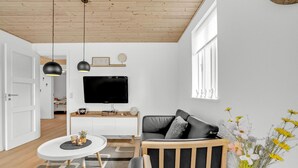 Ett modernt vardagsrum med en platt-TV, ett träpanelat tak och ett fönster med dekorativa ornament.