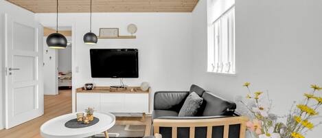 Una sala de estar moderna con un televisor de pantalla plana, techo de madera y un ventanal con adornos decorativos.
