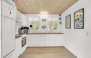 A modern kitchen with white cabinets, a wooden countertop, and a built-in oven. There are two windows with white frames, a sink, and a microwave on the counter.