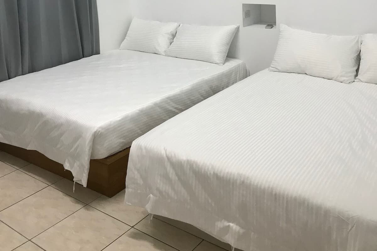 A hotel room with two single beds, a grey curtain, a blue accent wall, and a white ceiling.