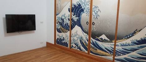 A room with a large sliding door featuring a wave painting, a flat-screen TV mounted on the wall, and wooden flooring.