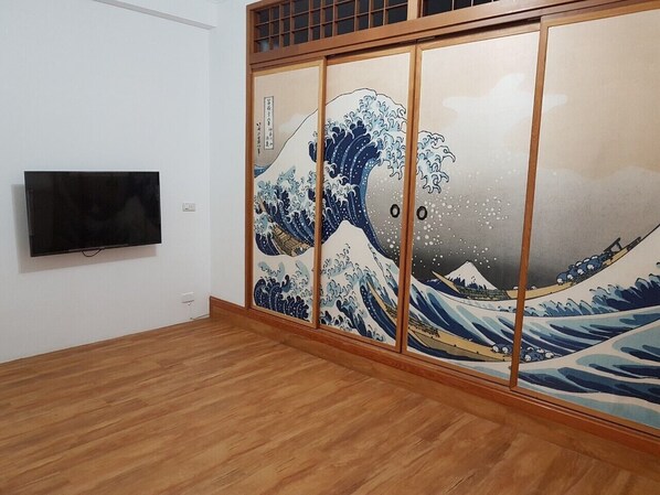 A room with a large sliding door featuring a wave painting, a flat-screen TV mounted on the wall, and wooden flooring.