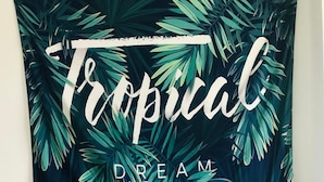 A room with a tropical-themed tapestry, a small table with two chairs, and a motivational sign. - Utopia Hostel (Taitung)
