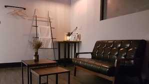 A living room with a leather sofa, a wooden coffee table, a ladder, and a small table with a vase. - Utopia Hostel (Taitung)