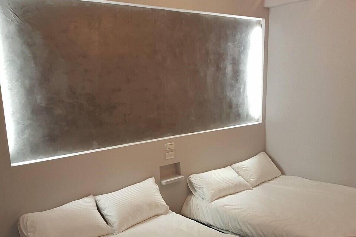 A modern bedroom with two beds, a large wall-mounted light, and a window.
