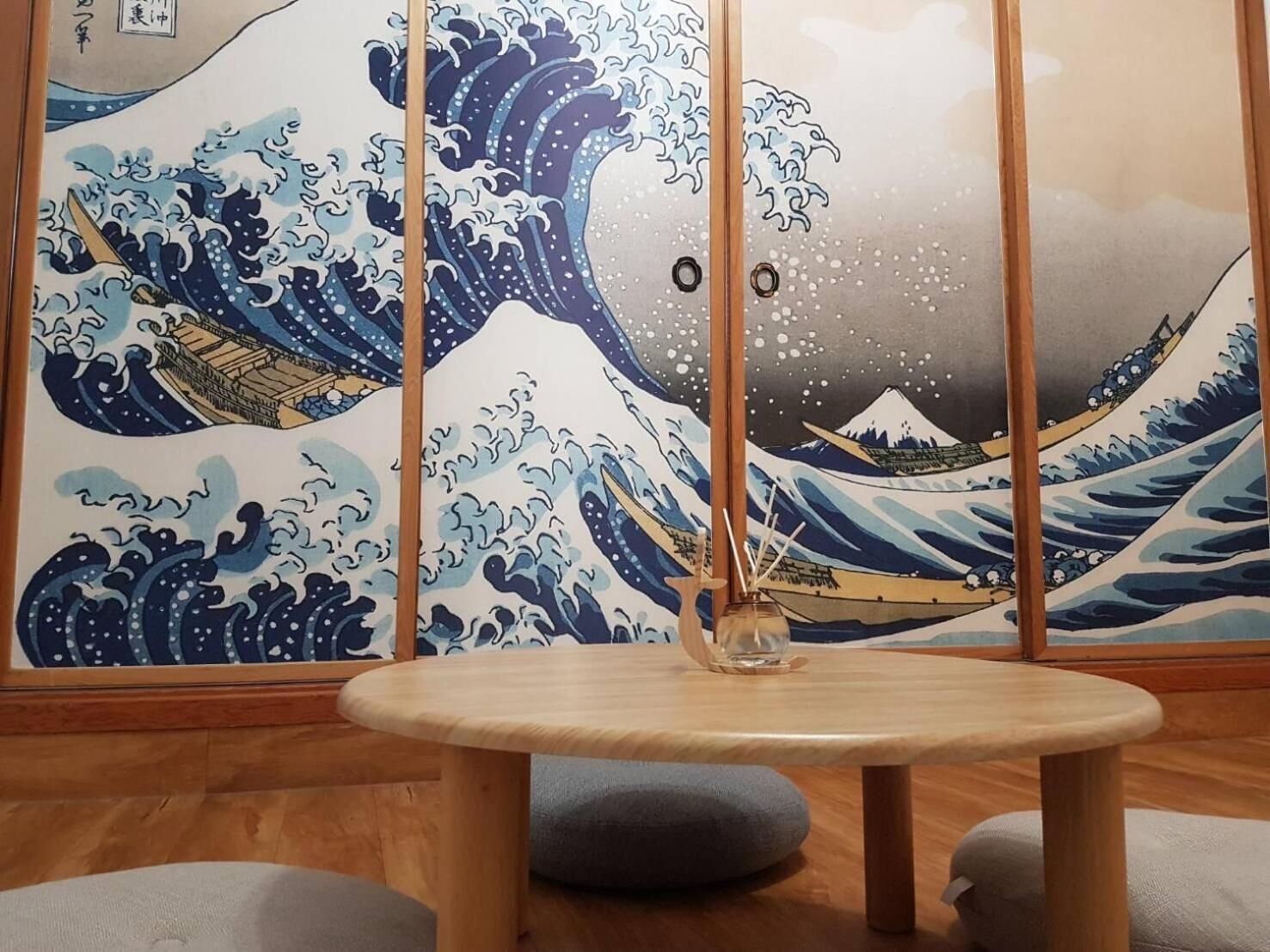 A room with a traditional Japanese wave painting on the wall, a round wooden table, and two cushions.