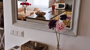 A mirror reflecting a dining area with a table, chairs, and a red lamp. A wicker basket and a vase with flowers are on a white console below the mirror. - bungalow - Formentera (La Savina)