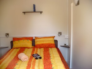 A bed with a striped bedspread, two pillows, a folded towel, and a book with sunglasses on it.