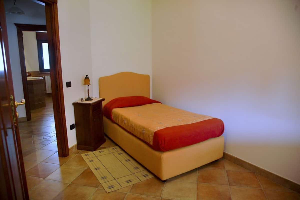 Un dormitorio pequeño con una cama individual, una mesita de noche y una puerta que da a otra habitación.