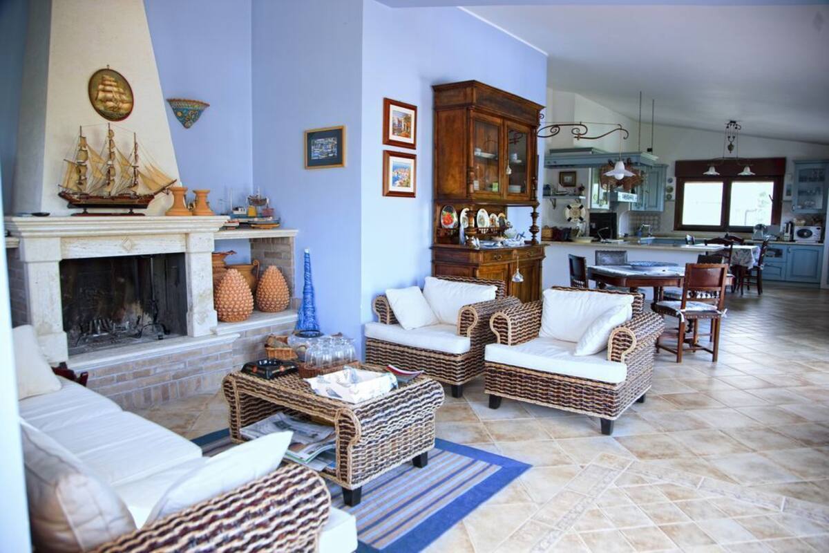 Una sala de estar con muebles de mimbre, una chimenea y una cocina al fondo.