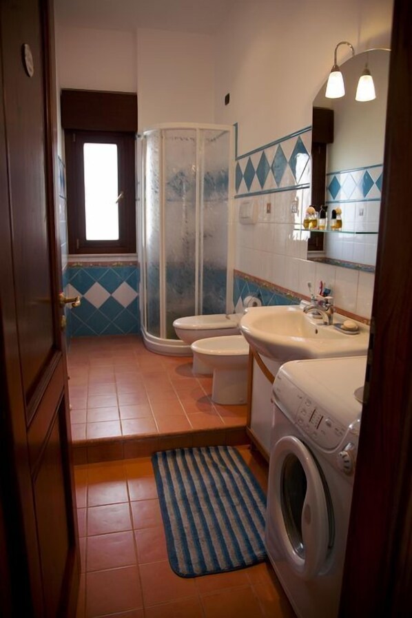 Un baño pequeño con ducha, dos inodoros, un lavabo y una lavadora.