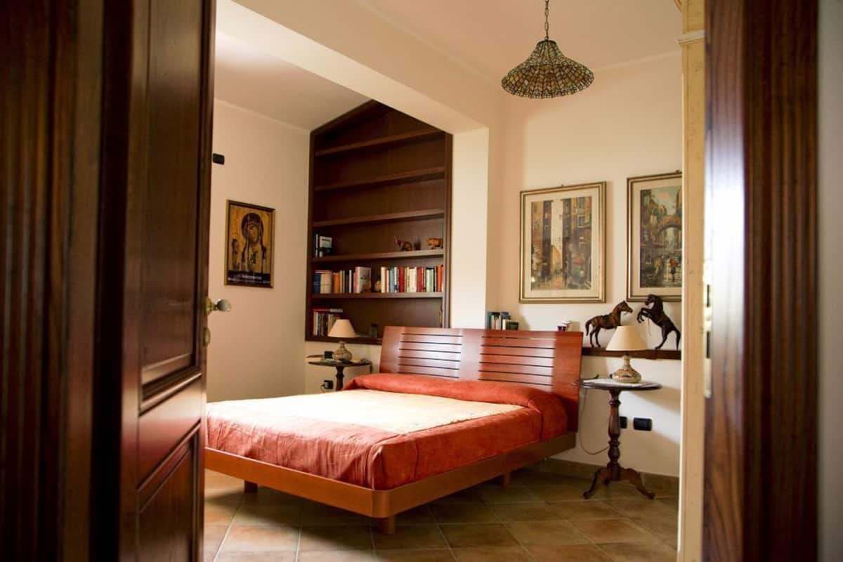 Un dormitorio con una cama de madera, una estantería y una mesita de noche con lámpara.