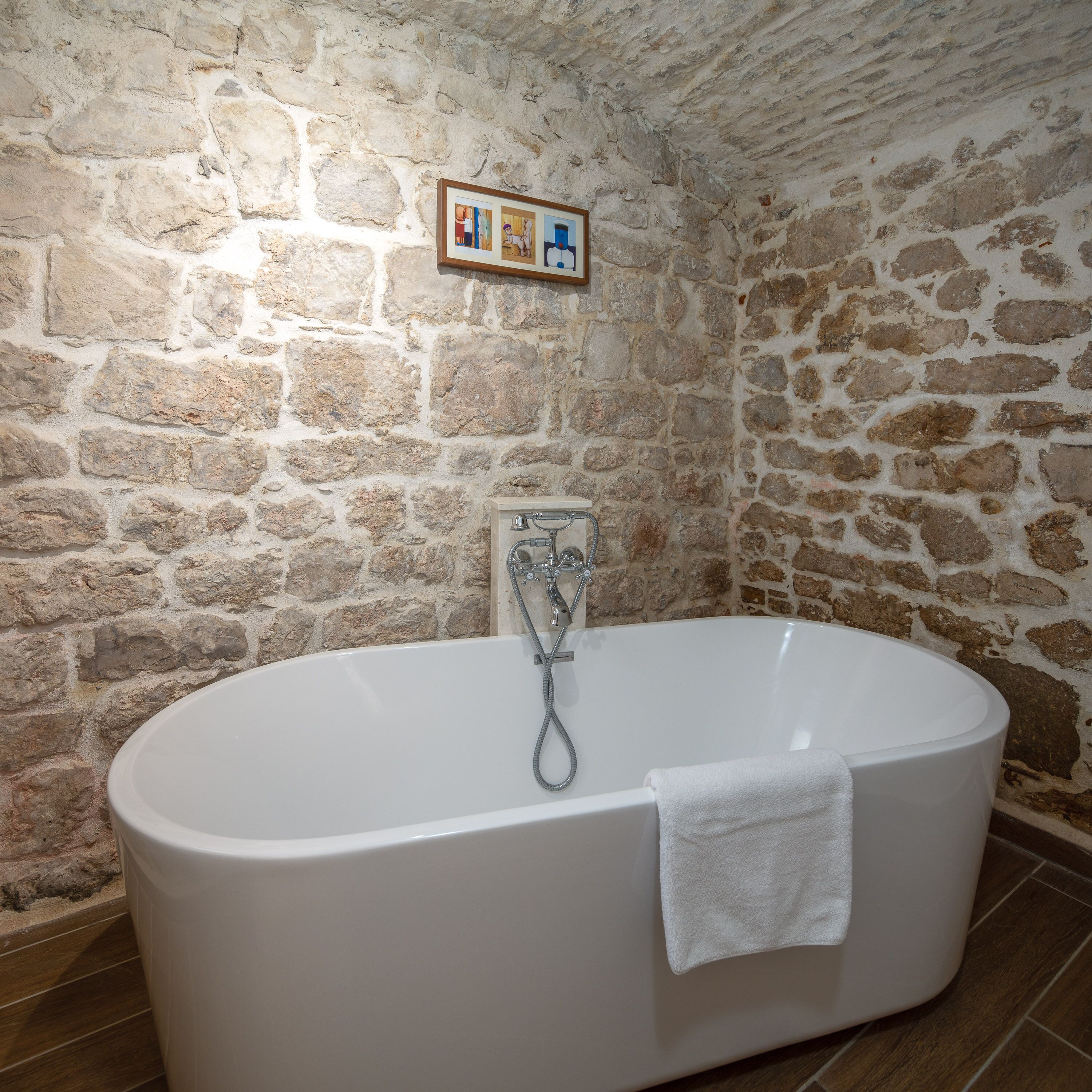 A stone-walled bathroom with a freestanding bathtub and a framed picture above it.