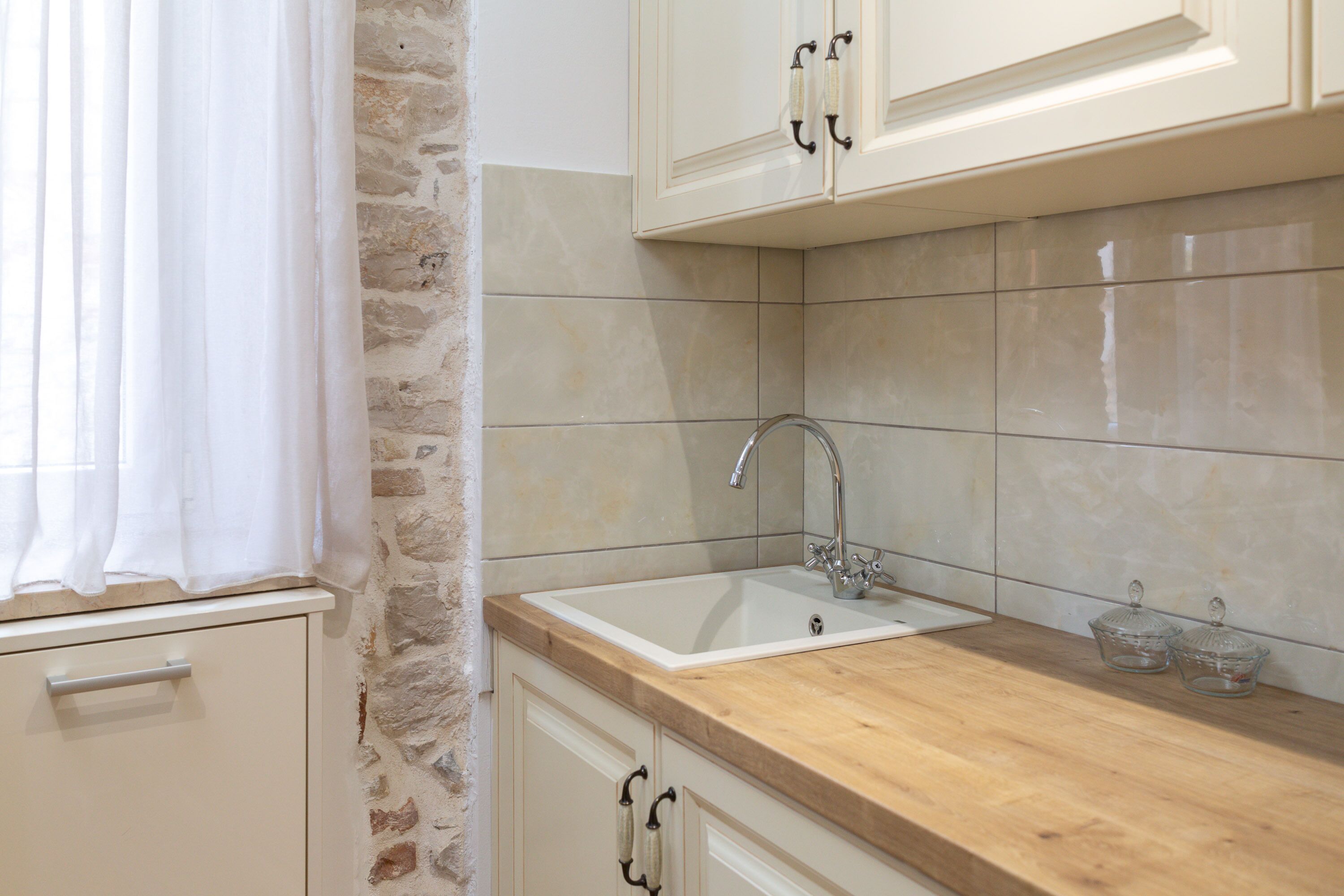 Una cucina con parete in pietra, pensili bianchi, piano di lavoro in legno e lavello.