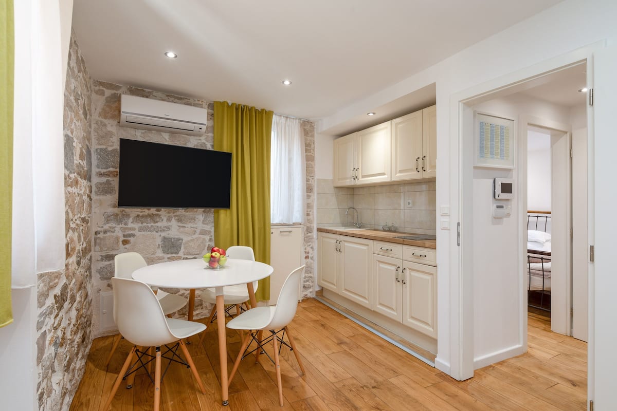 A modern kitchen with white cabinets, a stone accent wall, and a dining area with a round table and white chairs.