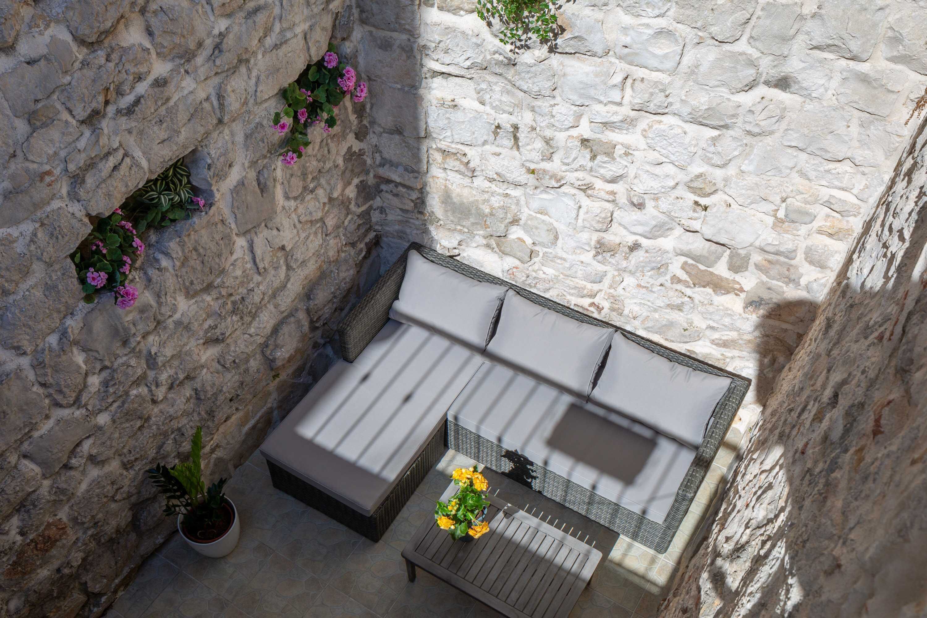 Habitación con paredes de piedra, una cama, una mesita pequeña y una planta en maceta.