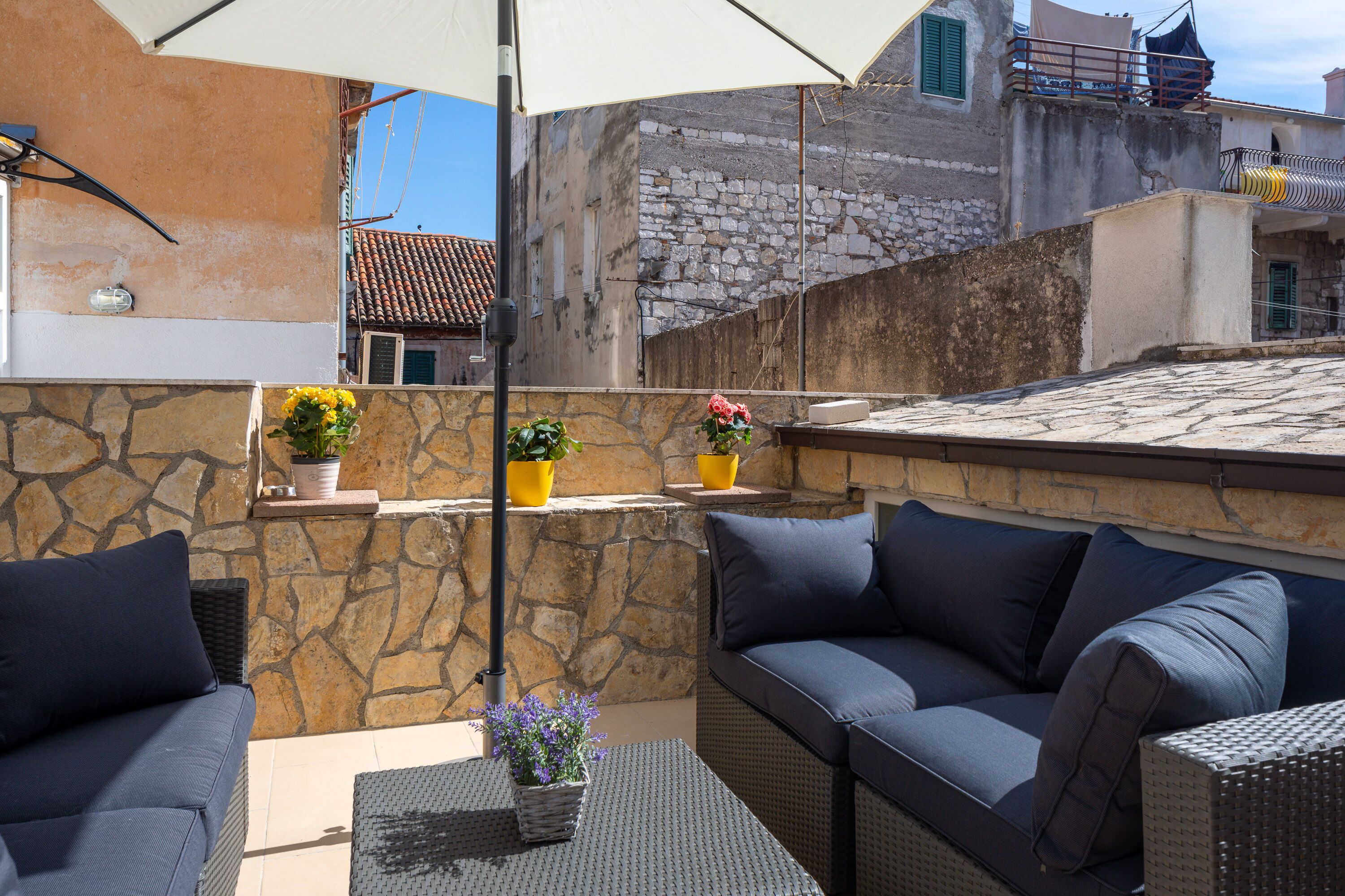 A rooftop terrace with outdoor seating, stone walls, and potted plants.