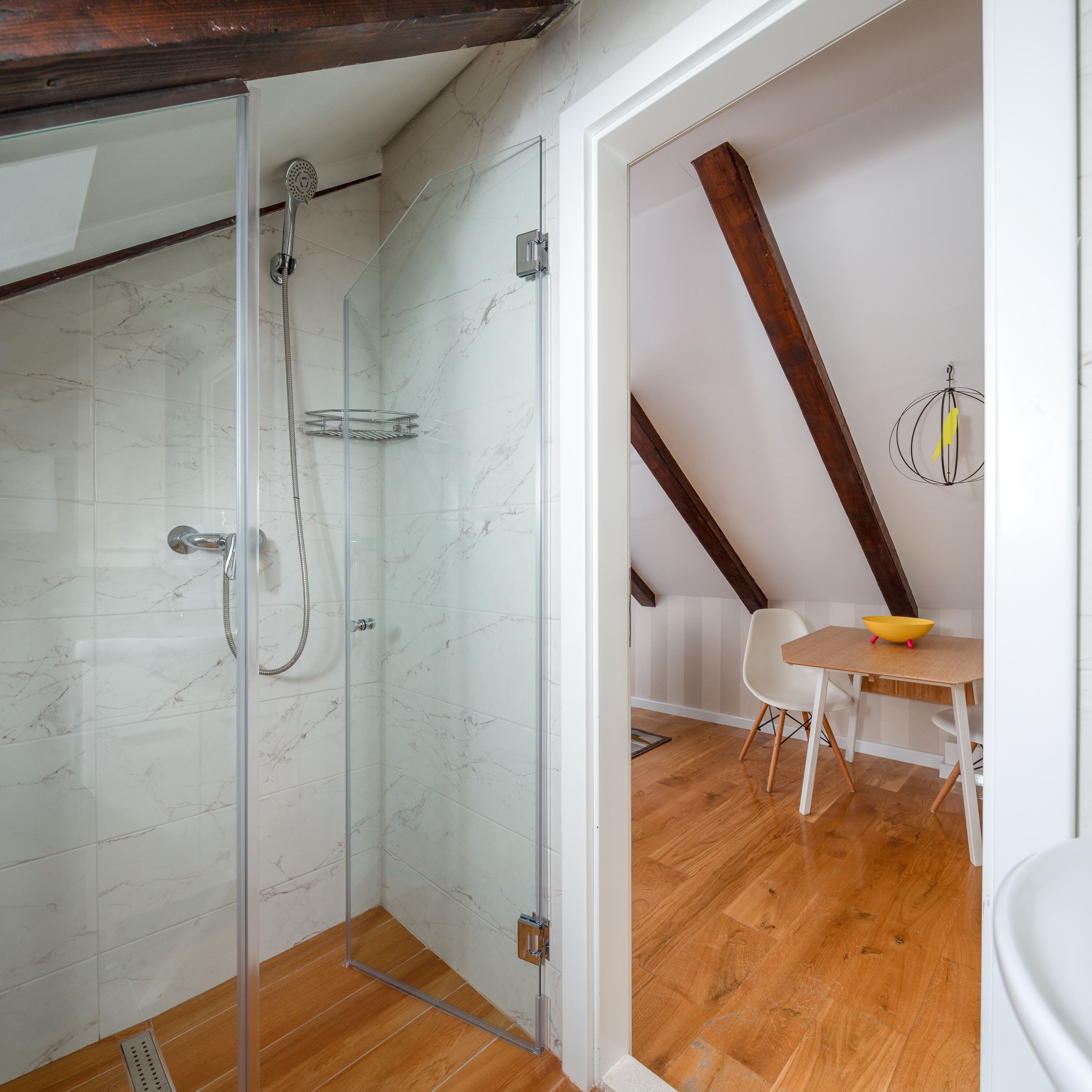 Un baño moderno con cabina de ducha de vidrio, paredes de mármol y suelo de madera.
