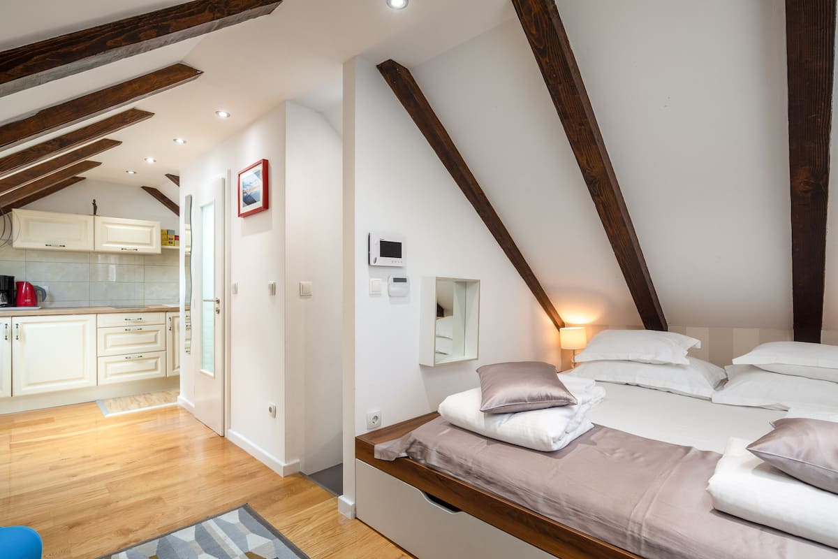 A bedroom with a loft-style ceiling, a bed with pillows, a bedside table, and a small bedside lamp.