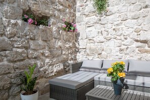 A stone wall with a wicker sofa and a table, a potted plant, and a vase with yellow flowers. - Awesome Stone House (Split)