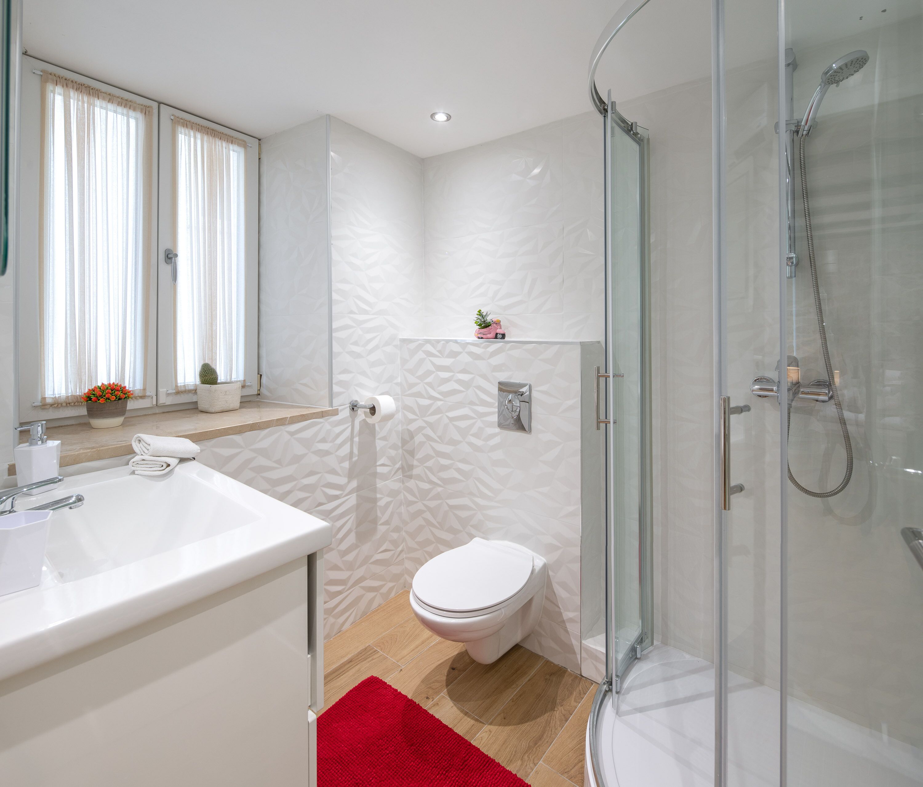 Un bagno moderno con box doccia in vetro, un water bianco e un lavandino con un tappetino da bagno rosso.