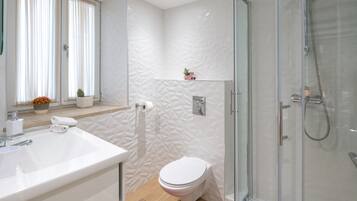 Un bany modern amb un espai de banyera de vidre, un vàter blanc i un lavabo amb un tapet de bany vermell.