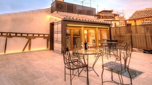 An outdoor patio with a glass table and metal chairs, a small building with a patterned door, and a tiled floor. - SYNAGOGUE 6 DELUXE WITH PRIVATE TERRACE (Toledo)