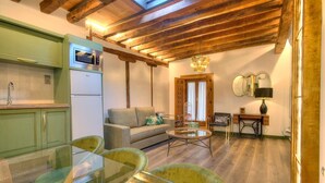 A cozy living area with a sofa, a glass coffee table, and a dining table with chairs. There is a kitchen with a microwave and a refrigerator. The room has wooden beams on the ceiling and a large window with curtains. - SYNAGOGUE 6 DELUXE WITH PRIVATE TERRACE (Toledo)