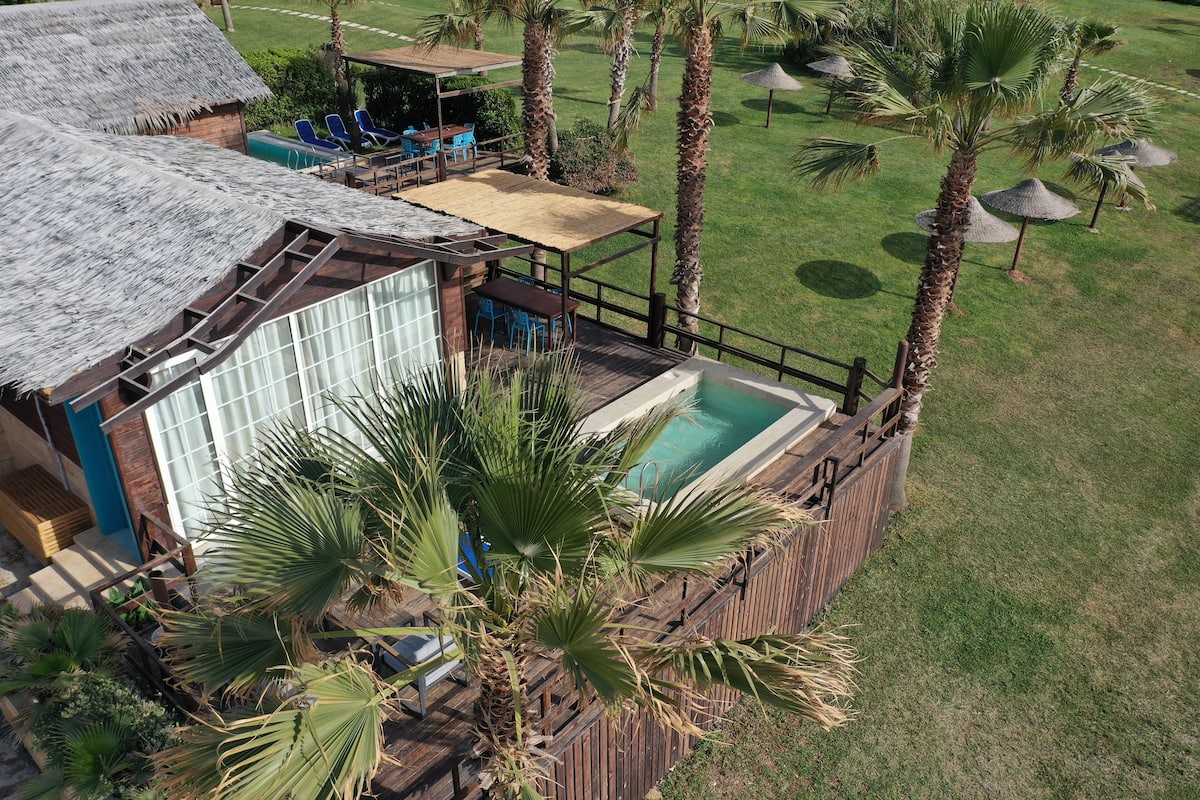 A resort with a pool, palm trees, and a thatched-roof structure.
