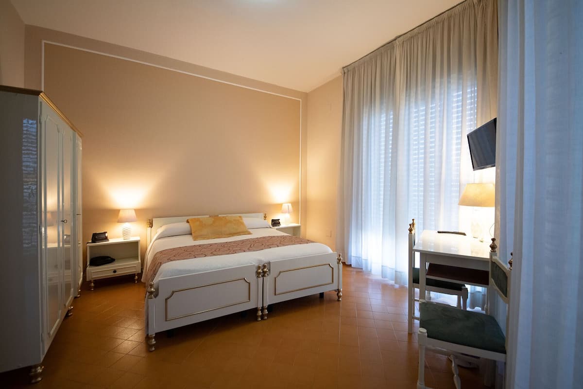 A hotel room with a bed, bedside lamps, a desk with a chair, and a television.