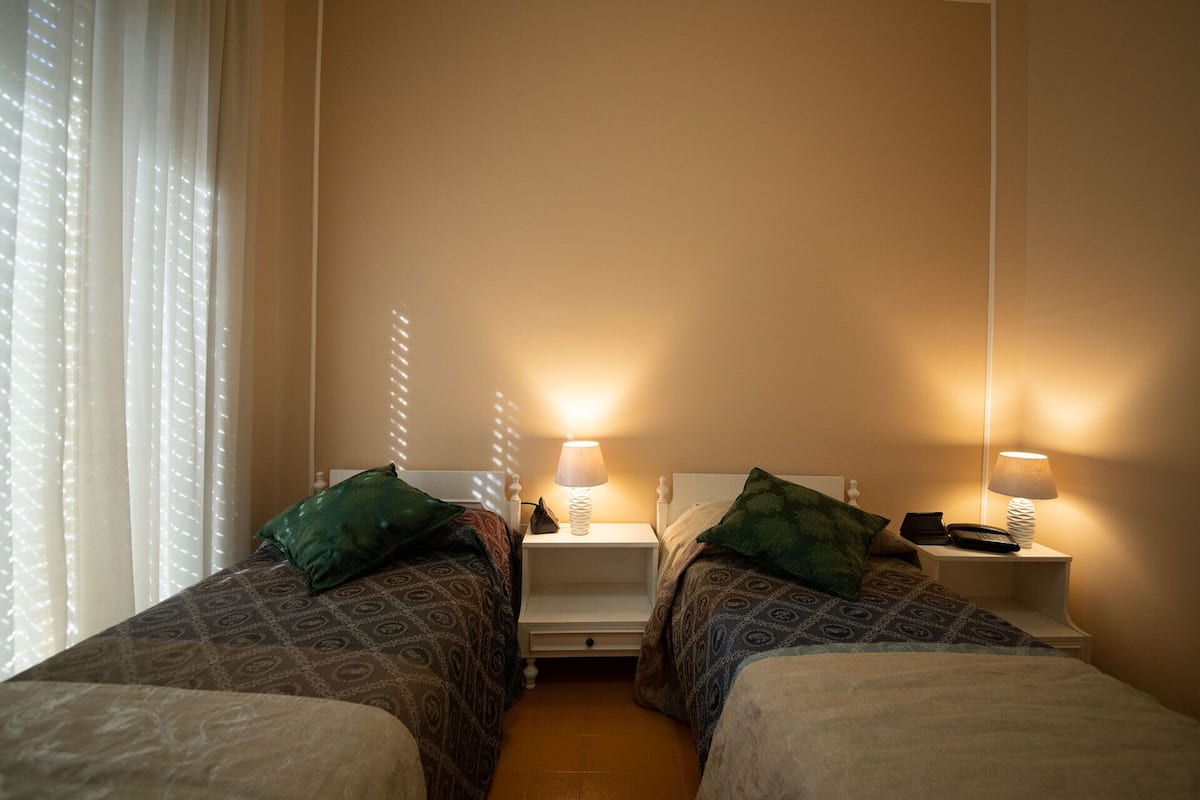 A twin room with two beds, each with a pillow and a bedside table with a lamp.