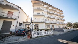 A multi-story residential building with balconies, a parked car, and a white fence. - Hotel Ristorante Venezuela (Montesano sulla Marcellana)