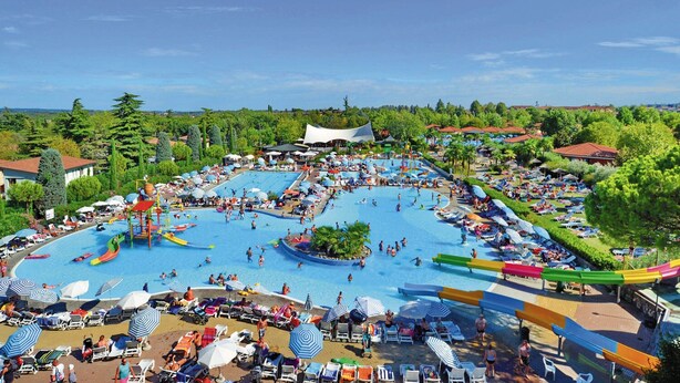 A large outdoor swimming pool complex with multiple water slides and a surrounding area with sun loungers and umbrellas.
