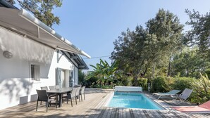 A wooden deck with a pool, lounge chairs, and a dining area. - Villa Takamira - heated pool and spacious garden close to Golf and Beaches (Soorts-Hossegor)
