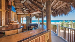 A wooden bar area with a thatched roof, overlooking a beach.