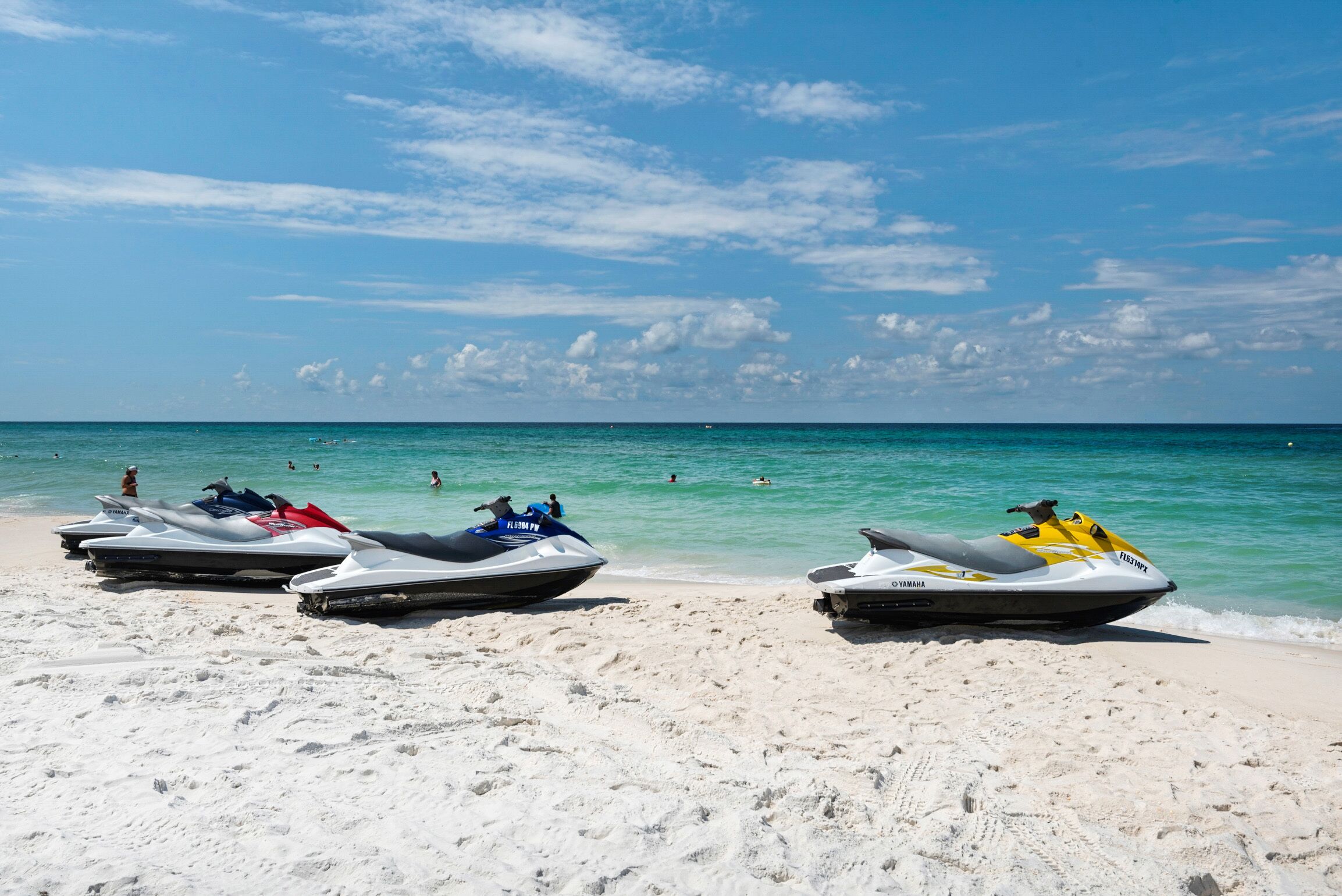 Jet skis parked on a sandy beach with the ocean in the background.