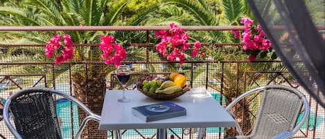 A balcony with two wicker chairs, a table with a fruit bowl, a wine glass, and a book.