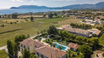 Un complejo turístico en la costa con varias edificaciones, piscina y vista al mar y a las montañas.