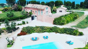 Une grande villa rose dotée d’une piscine et de chaises longues, entourée d’une végétation luxuriante et offrant une vue sur la mer.