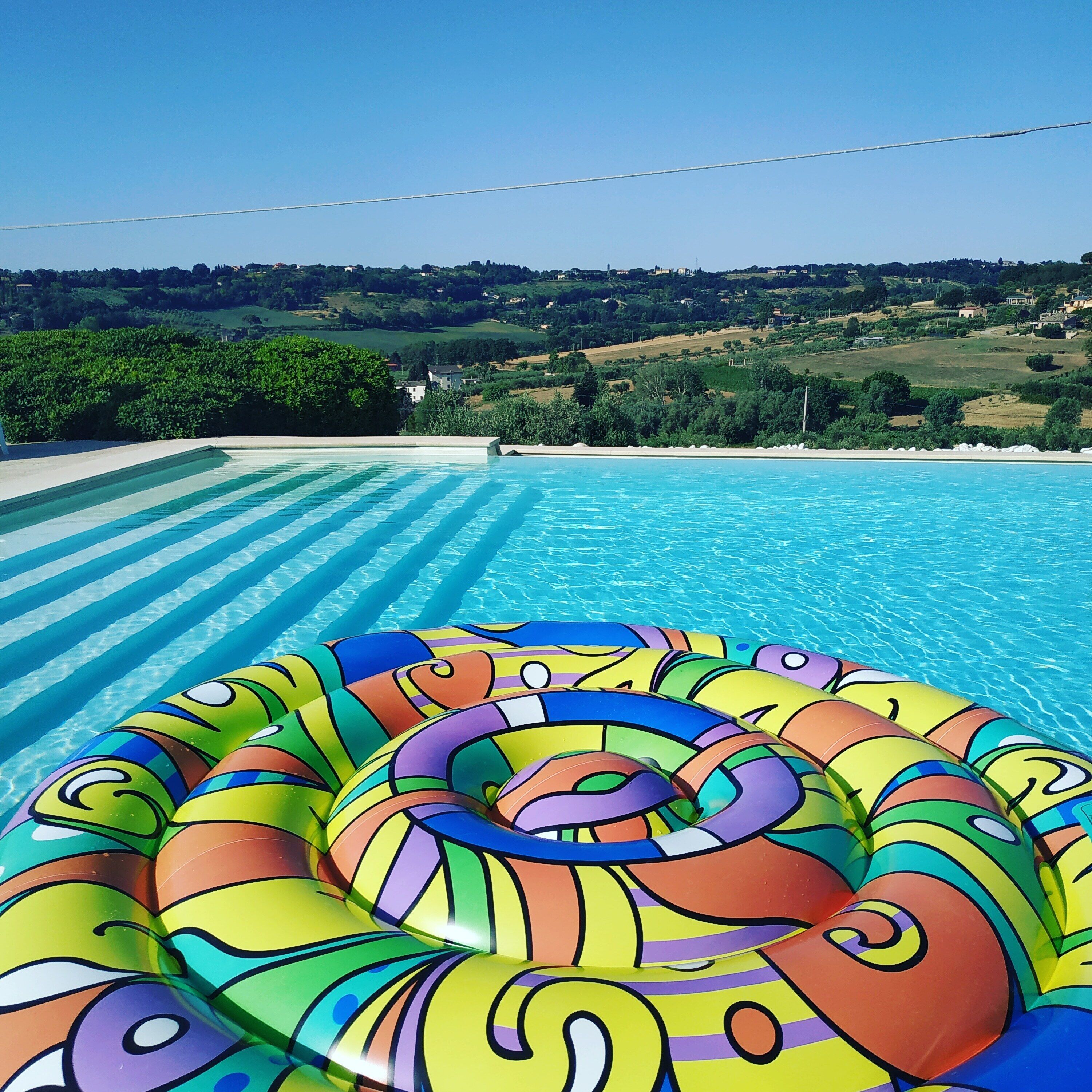 Una piscina con acqua cristallina e un colorato materassino gonfiabile in primo piano.