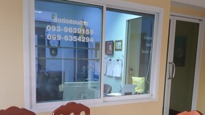 Un comedor con una mesa redonda y sillas de madera, una ventana con números de contacto y una puerta con manija.