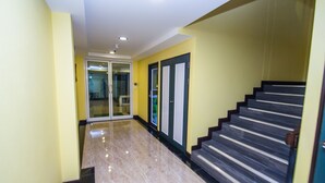 Un pasillo con piso de mármol, una escalera con escalones oscuros y una puerta de cristal que da a otra habitación.