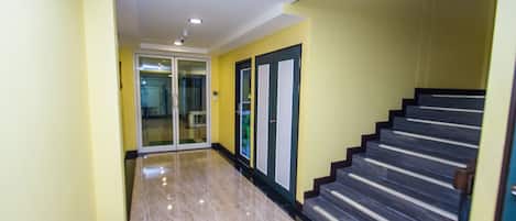 A hallway with a marble floor, a staircase with dark steps, and a glass door leading to another room.