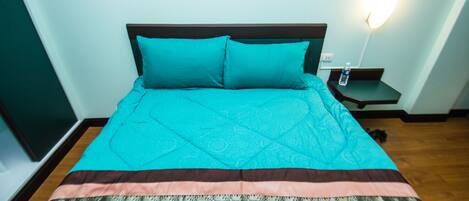A neatly made bed with a patterned bedspread and pillows, a bedside table with a water bottle, and a wall-mounted light fixture.