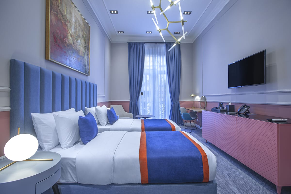 A hotel room with two beds, a desk, a TV, and a painting on the wall.
