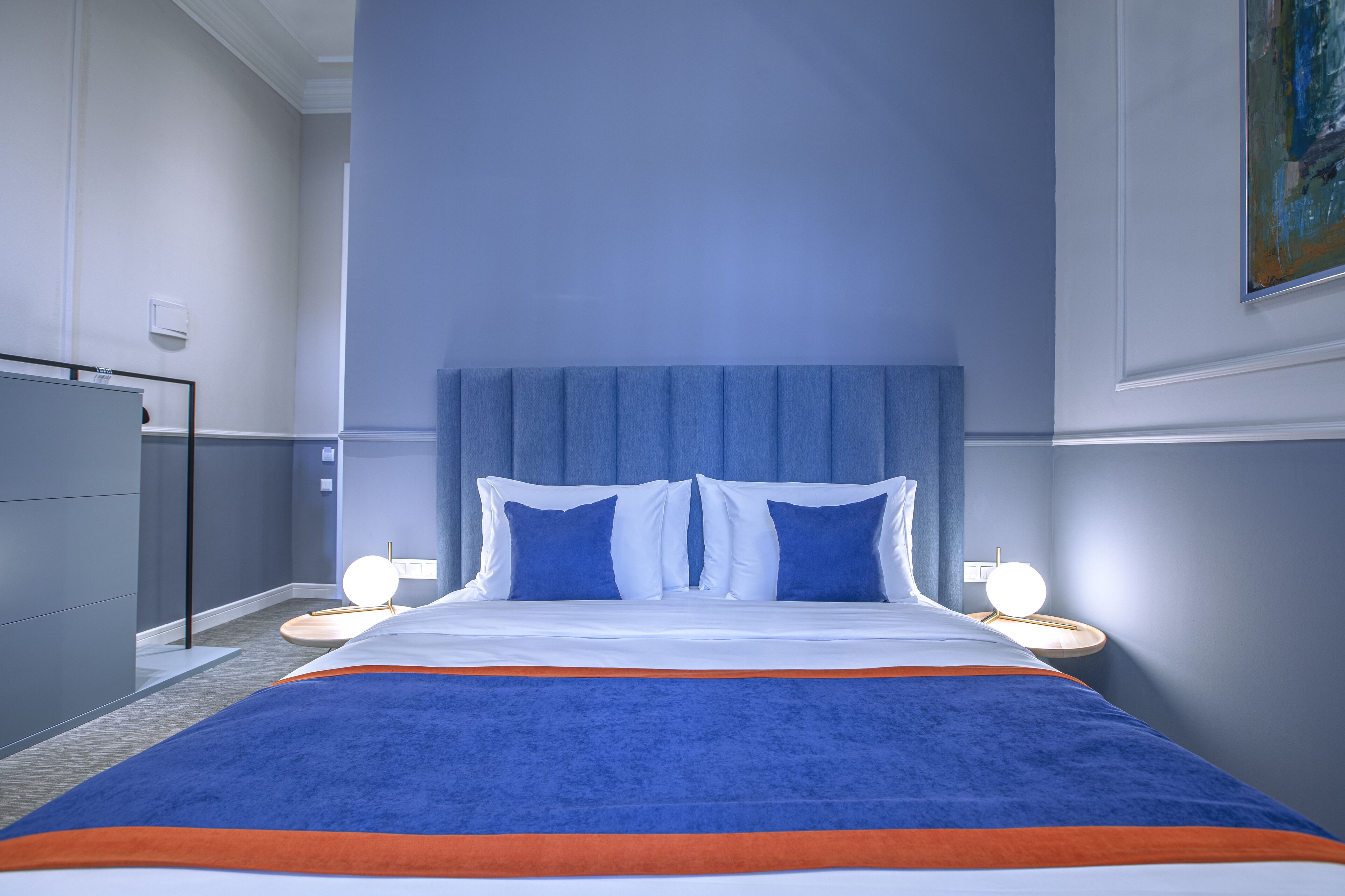A hotel room with a large bed, two bedside tables with lamps, a dresser, and a painting on the wall.