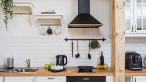 Une cuisine avec des armoires blanches, un plan de travail en bois, une hotte noire et divers ustensiles et appareils de cuisine.